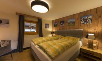 A cozy bedroom with a double bed and checkered blankets. The wooden paneling and the pictures on the wall give the room a warm atmosphere.