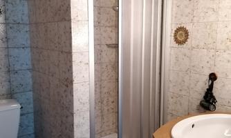 A bathroom with a shower cubicle and a washbasin. The walls are decorated with light tiles.