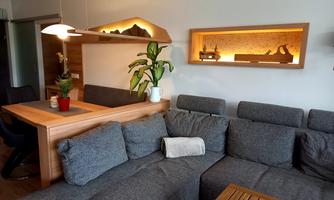 A modern living room with a gray sofa and a wooden table. A plant and decorative elements on shelves create a cozy atmosphere.
