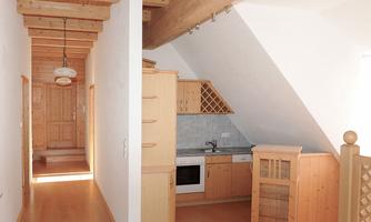 A cozy kitchen with wooden cabinets and modern appliances. The room has a bright atmosphere due to large windows and wooden ceilings.