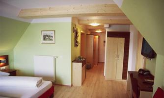 A cozy room with two beds and light green walls. The room features a television and a wooden wardrobe.