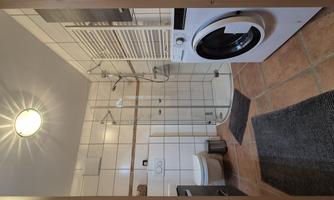 A modern bathroom with a shower and a washing machine. The room is bright and well-equipped.