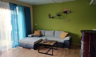 A bright living room with a gray sofa and colorful cushions. On the wall is a modern shelf, and large windows provide plenty of daylight.