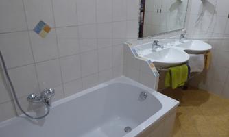 A bathroom with a bathtub and two sinks. The walls are brightly tiled, and there are towels at the sinks.