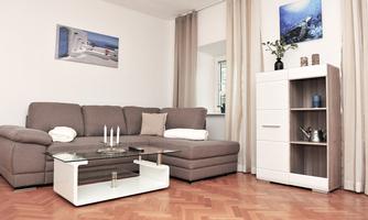 A modern living room with a cozy sofa and a glass coffee table. A picture hangs on the wall and a shelf stands next to a window.
