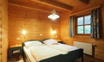 A cozy bedroom with two beds and wooden paneling. The room has warm lighting and a window with curtains.