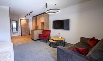 A modern living room with a cozy sofa and a round table. The decor is simple and stylish, with a view of an open kitchen.
