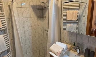 A modern bathroom with a shower and a wooden shelf. The space is clean and well-lit, with towels and personal care products.