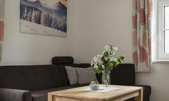 A cozy living room with a brown sofa and a wooden table. On the table, there is a flower vase and a landscape painting hangs on the wall.