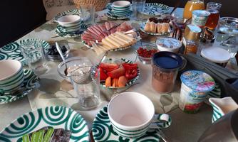 A table, richly set with various foods such as sausage, cheese, fruit, and chocolate. There are also drinks and decorative dishes in a green pattern.