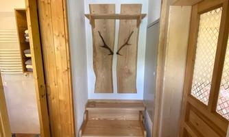 A cozy entrance area with wooden paneling and a simple seating area. Modern wooden coat hooks hang on the wall.