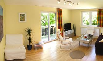 A bright living room with yellow walls and large windows. It is decorated with modern furniture and plants and has an inviting, cozy character.