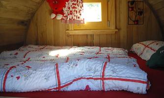 A cozy bedroom with wooden paneling and a window. There are two beds with colorful bedspreads and decorative furnishings.