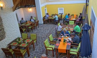 A cozy courtyard scene with wooden tables and chairs. Guests are sitting together relaxed and enjoying their meals in a friendly atmosphere.