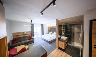 A modern hotel room with a comfortable sofa and a large bed.  
The room is bright and inviting, with a shower and windows that offer a view outside.