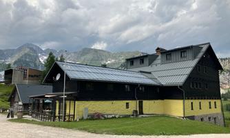 A modern building in black and yellow, surrounded by green meadows and mountains. The sky is overcast, creating a calm atmosphere.