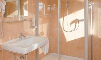 A modern bathroom with a shower and a sink. The walls are light tiled and there are large mirrors.