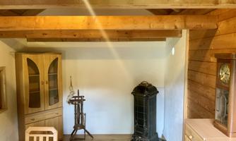 A cozy room with wooden ceilings and furniture. In the corner stands a classic stove and a wall clock.