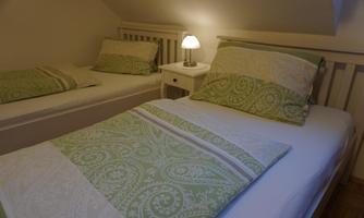 A simple bedroom with two beds and pretty green bedding. A bedside table with a lamp stands between the beds.