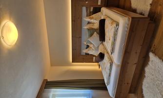 A cozy bedroom with a double bed and wooden details. The windows let in plenty of light and the floor is covered with soft carpets.