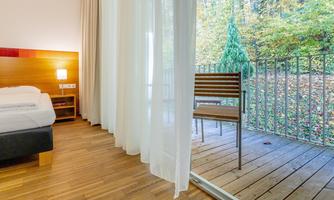 A cozy room with wooden floors and a view of a balcony. Outside, trees and fresh nature can be seen.