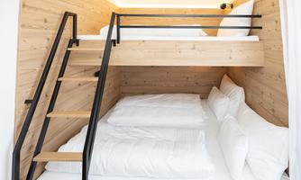 A modern bedroom with a bunk bed and a double bed. The walls are made of light wood, and the room feels cozy and welcoming.