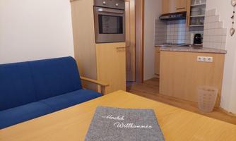 A cozy apartment with a blue couch and a dining area. The kitchen is modern and well-equipped.