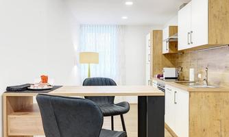 A modern residential kitchen with a small dining table and two chairs. The room has a bright atmosphere with natural light.