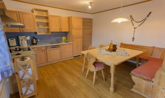 A bright kitchen with wooden cabinets and a dining area. A decorative tablecloth is on the table and some drinks are visible.