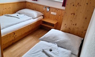 A simple room with two beds and wooden walls. There is a window with a view and red curtains.