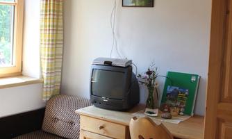 A small room with a television, a desk, and a cozy sofa. The window lets in a lot of daylight and there is a beautiful wall decoration.
