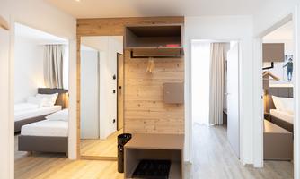 A modern room with wooden elements and a large mirror. There are two bedrooms connected by an open entrance door.
