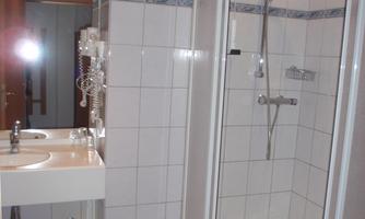 A bathroom with a shower cabin and a sink. The walls are tiled and the floor is light blue.