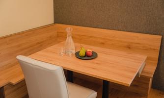 A wooden table with a white chair is located in a cozy corner. On the table, there is a carafe and a bowl of apples and pears.
