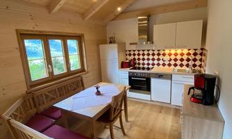 A modern kitchen with wooden furniture and a cozy dining area. Large windows offer a beautiful view outside.