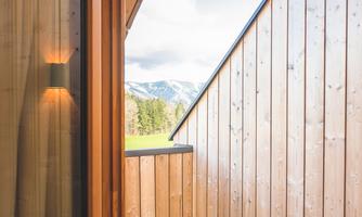 A cozy balcony with wooden walls and a clear sky. Gentle mountains can be seen in the background.