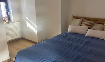 A bright bedroom with a large bed and pillows. The walls are white and the floor is wooden.