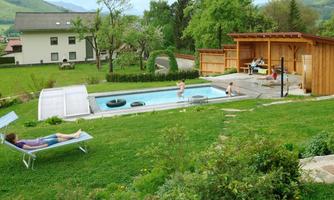 A beautiful garden with a swimming pool and a lounge chair. In the background, there are trees and a wooden shed.