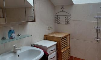 A bathroom with a sink, a mirror, and a window. There is also a laundry basket made of rattan and a shelf holder on the wall.