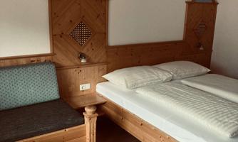 A cozy bedroom with a double bed and a wooden seating area. The walls are decorated with wood paneling and decorative elements.