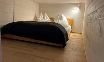 A cozy bedroom with a double bed. The walls are light and made of wood, and the floor is made of light wood.