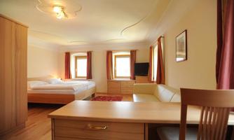 A bright bedroom with a large bed, a seating area, and a desk. The walls are in neutral colors, with wooden and fabric elements.