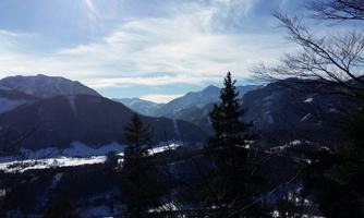 A picturesque mountain landscape with snow-covered slopes and clear blue sky. In the foreground, there are some trees that complement the magnificent view.