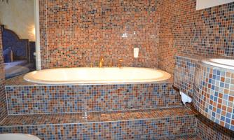 A stylish bathroom with a large bathtub on an elevated platform. The walls are decorated with colorful mosaic tiles.