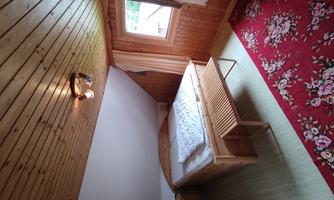 A cozy bedroom with wooden walls and a sloped ceiling. There is a large bed, a small table, and a carpet with a floral pattern.