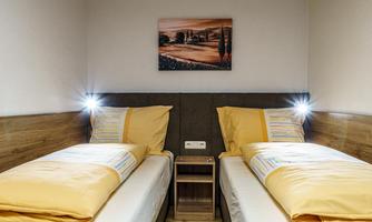 A cozy bedroom with two single beds and yellow bedspreads. A picture of a landscape hangs on the wall, and there are small bedside lamps.