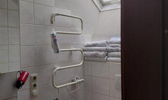 A small bathroom with white tiles and a skylight. Towels are neatly stacked and a toilet paper holder is visible.