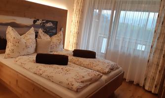 A cozy bedroom with a large bed and wooden furniture. Large windows provide plenty of daylight and a view outside.