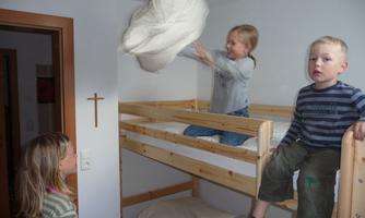 Three children are playing in a room with a bunk bed. One child is throwing a blanket in the air while the others watch.