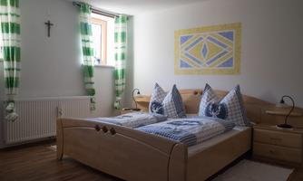 A cozy bedroom with two beds and bright wall decoration. The windows are adorned with striped curtains and there is a small bedside lamp.